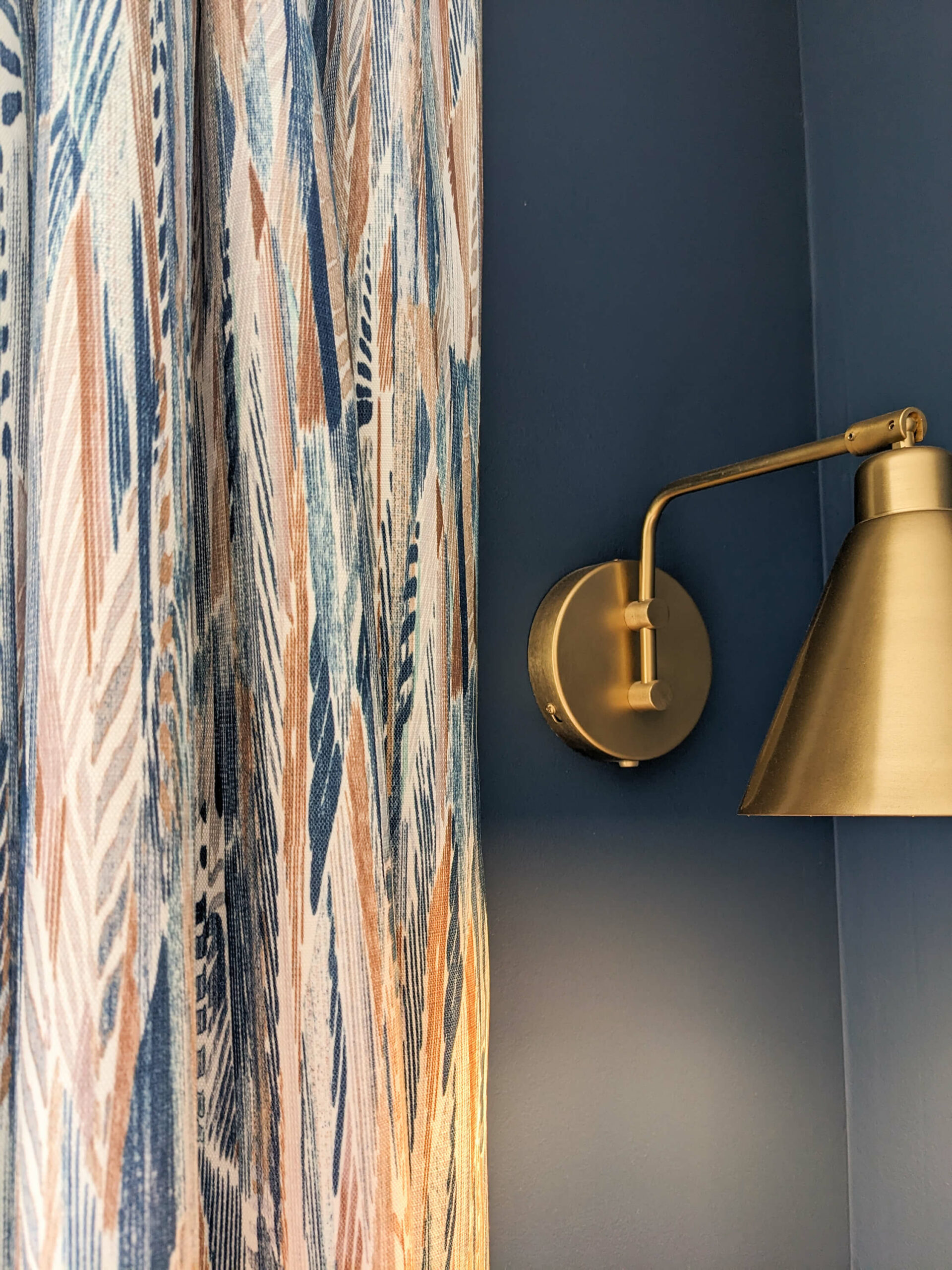 Domaine de Prestal rénovation maisons d'hotes chambre Rénovation d’une maison ancienne en chambre d’hôtes au Merlerault dans le perche normand, avec des rideaux en tissu ethnique de plumes bleu et marron, un mur bleu foncé et une applique rétro en laiton