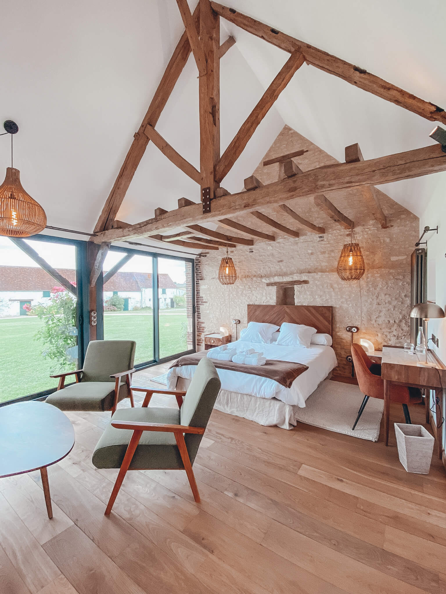 Domaine de Prestal rénovation ancien four à pain photo de réalisation Réhabilitation d'un ancien four à pain en chambre d'hôtes chaleureuse avec poutres apparentes, lumière naturelle, mobilier en bois massif, marbre blanc et laiton, suspension en fibres naturelles, fauteuil en bois massif avec tissu vert nature, au Merlerault dans le perche normand