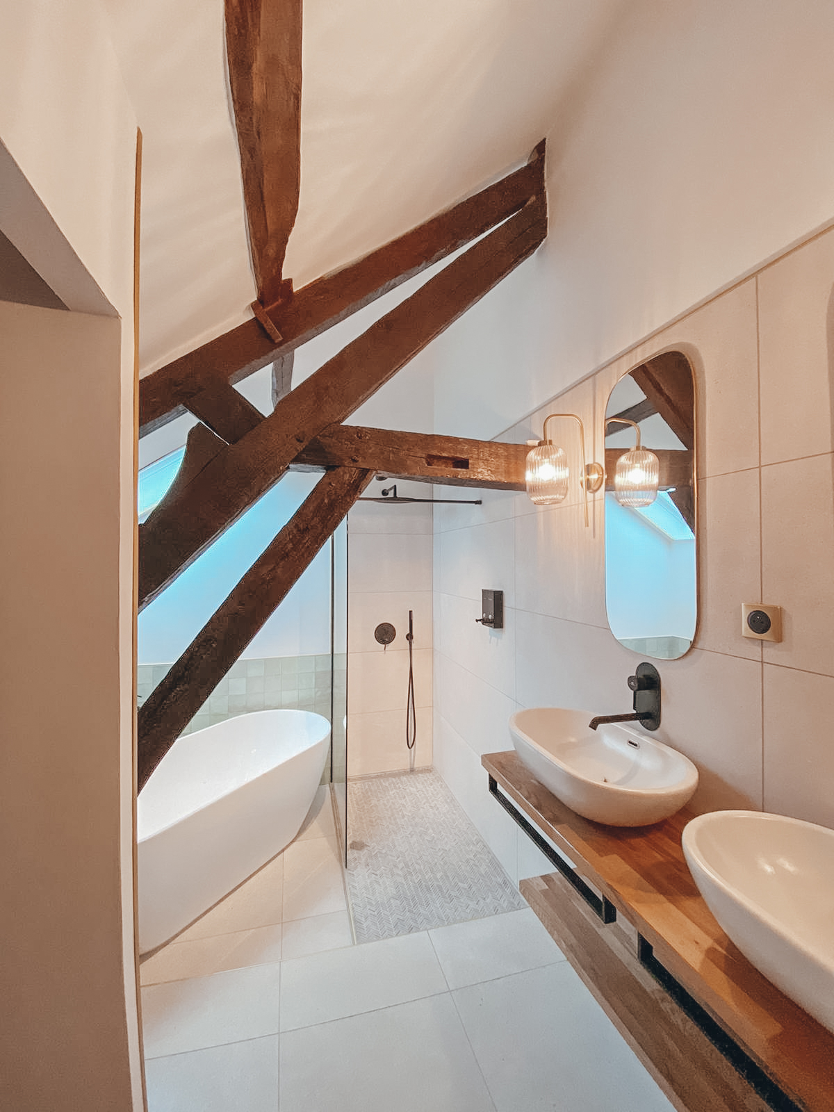 Domaine de Prestal rénovation maisons d'hotes salle de bain Rénovation d’une maison ancienne en chambre d’hôtes au Merlerault dans le perche normand, salle de bain avec baignoire ilot entourée de zelliges vert pastel aux murs, douche à l’italienne, plan double vasque bois, vasque à poser blanche, appliques en verre et laiton