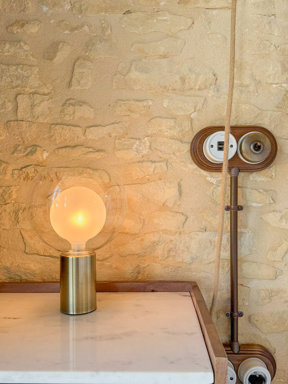 Domaine de Prestal rénovation ancien four à pain détail lampe chevet et mur de pierre Réhabilitation d'un ancien four à pain en chambre d'hôtes chaleureuse avec détail sur la lampe de chevet en laiton et verre, table de chevet en bois massif avec plateau de marbre blanc, appareillage électrique en bois et porcelaine, au Merlerault dans le perche normand