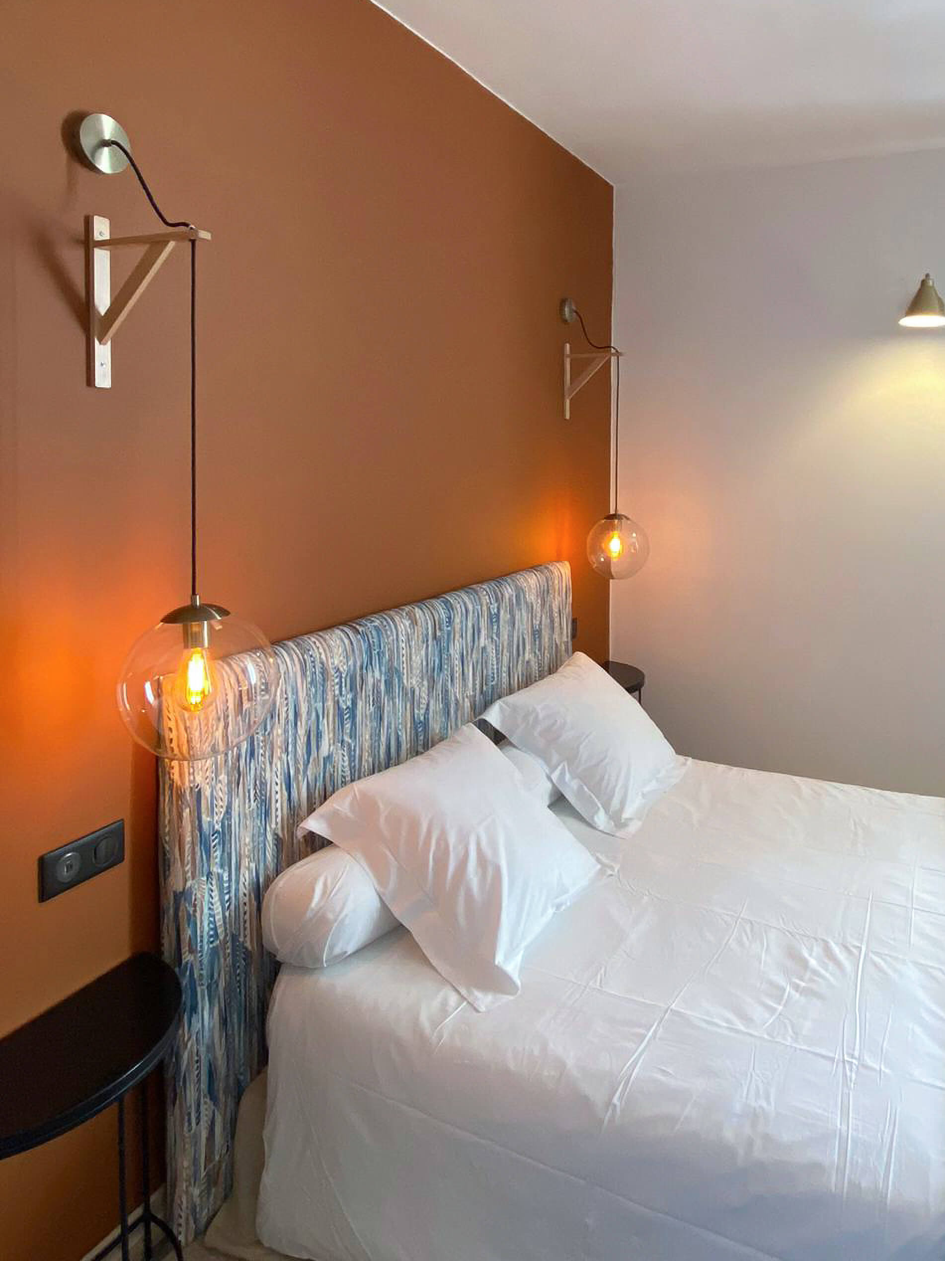 Domaine de Prestal rénovation maisons d'hote, chambre, tete de lit ethnique, mur ton terre cuite, suspension laiton et verre, chevet métal noir Rénovation d’une maison ancienne en chambre d’hôtes au Merlerault dans le perche normand, avec une tête de lit en tissu ethnique de plumes bleu et marron, un mur couleur terre cuite et des suspensions modernes en verre et laiton, chevet métal noir