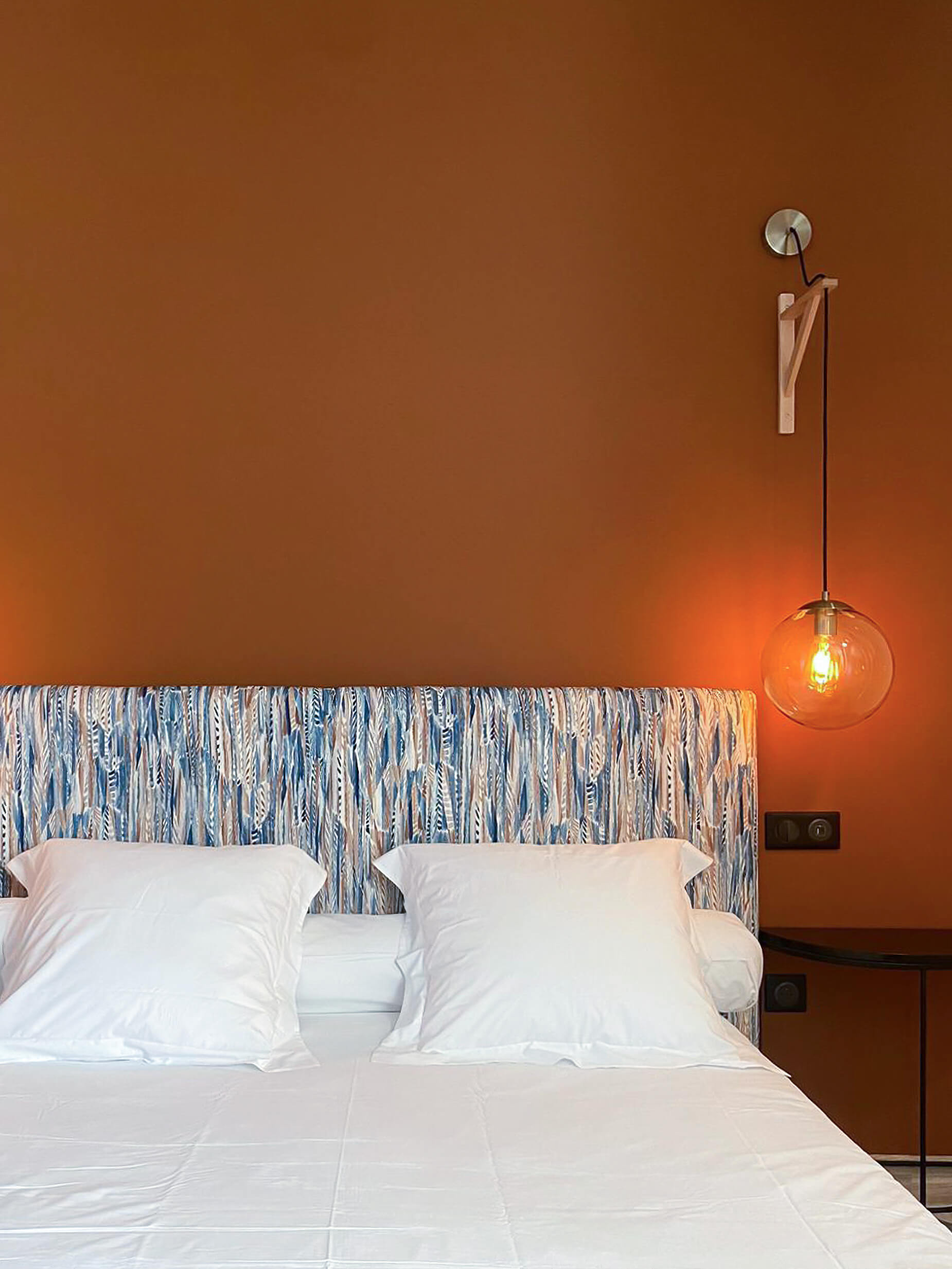 Domaine de Prestal rénovation maisons d'hote, chambre, tete de lit ethnique, mur ton terre cuite, suspension laiton et verre Rénovation d’une maison ancienne en chambre d’hôtes au Merlerault dans le perche normand, avec une tête de lit en tissu ethnique de plumes bleu et marron, un mur couleur terre cuite et des suspensions modernes en verre et laiton, chevet métal noir