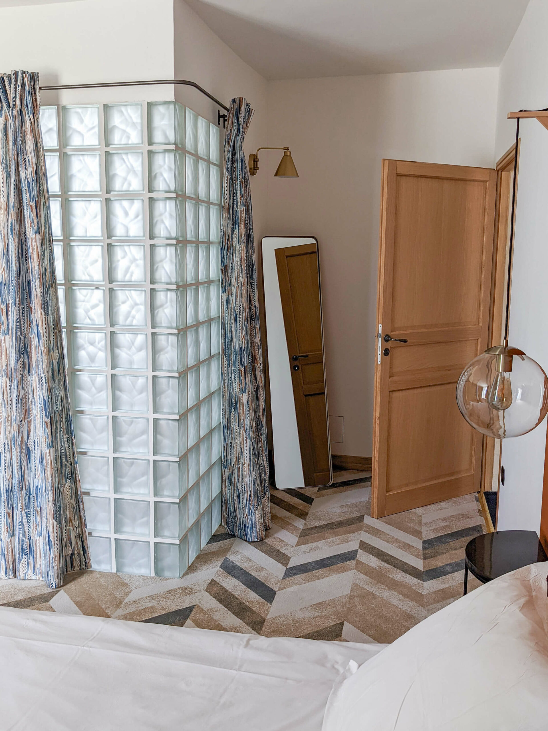 Domaine de Prestal rénovation maisons d'hotes chambre, moquette chevron, rideaux tissu ethnique, carreaux de verre, luminaires laiton Rénovation d’une maison ancienne en chambre d’hôtes au Merlerault dans le perche normand, avec des rideaux en tissu ethnique de plumes bleu et marron, un mur en carreaux de verre pour séparer la salle de bain