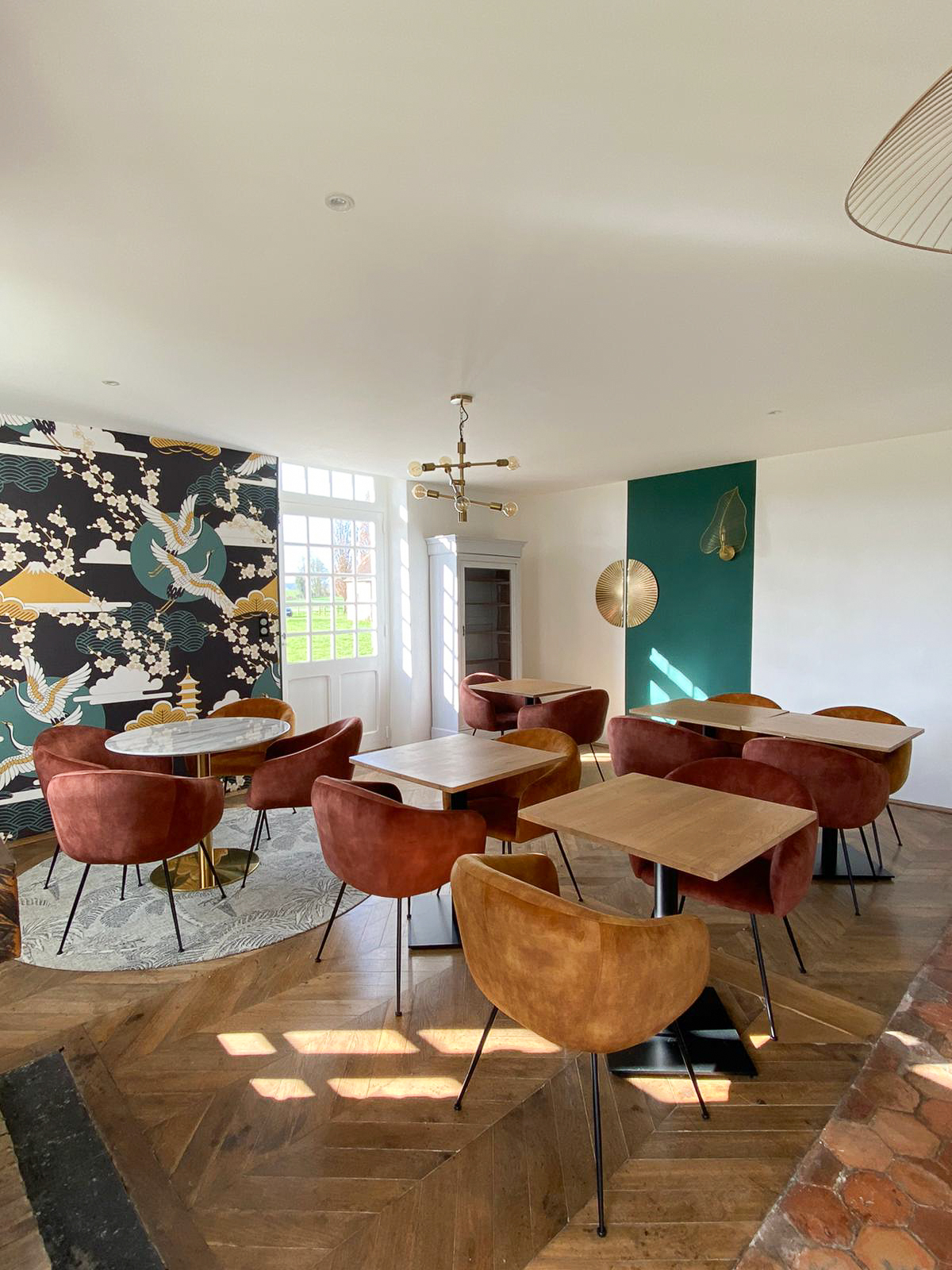 Domaine de Prestal rénovation maisons d'hotes, salle du petit déjeuner lumineuse et colorée Rénovation d’une maison ancienne en chambre d’hôtes au Merlerault dans le perche normand, salle du petit déjeuner avec un papier peint japonisant, du parquet massif et des tomettes anciennes, tables en bois et fauteuils de table colorés, détails en laiton