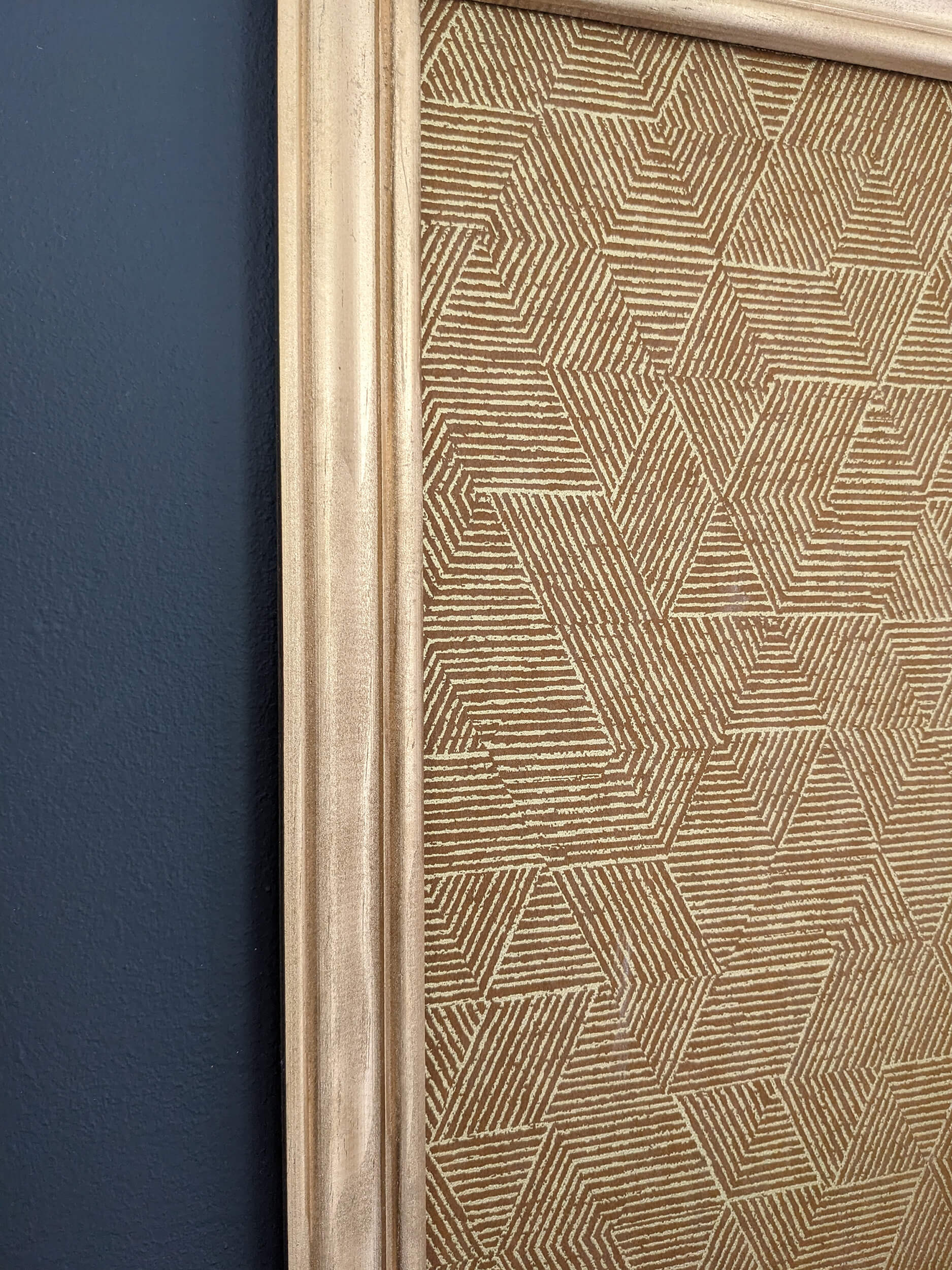 Rénovation d’une maison ancienne en chambre d’hôtes, détail tête de lit avec moulures doré et papier peint géométrique mordoré Rénovation d’une maison ancienne en chambre d’hôtes au Merlerault dans le perche normand, esprit art déco avec une tête de lit en papier peint à motifs géométriques dorés encadré par des moulures dorées, le tout sur un mur gris foncé