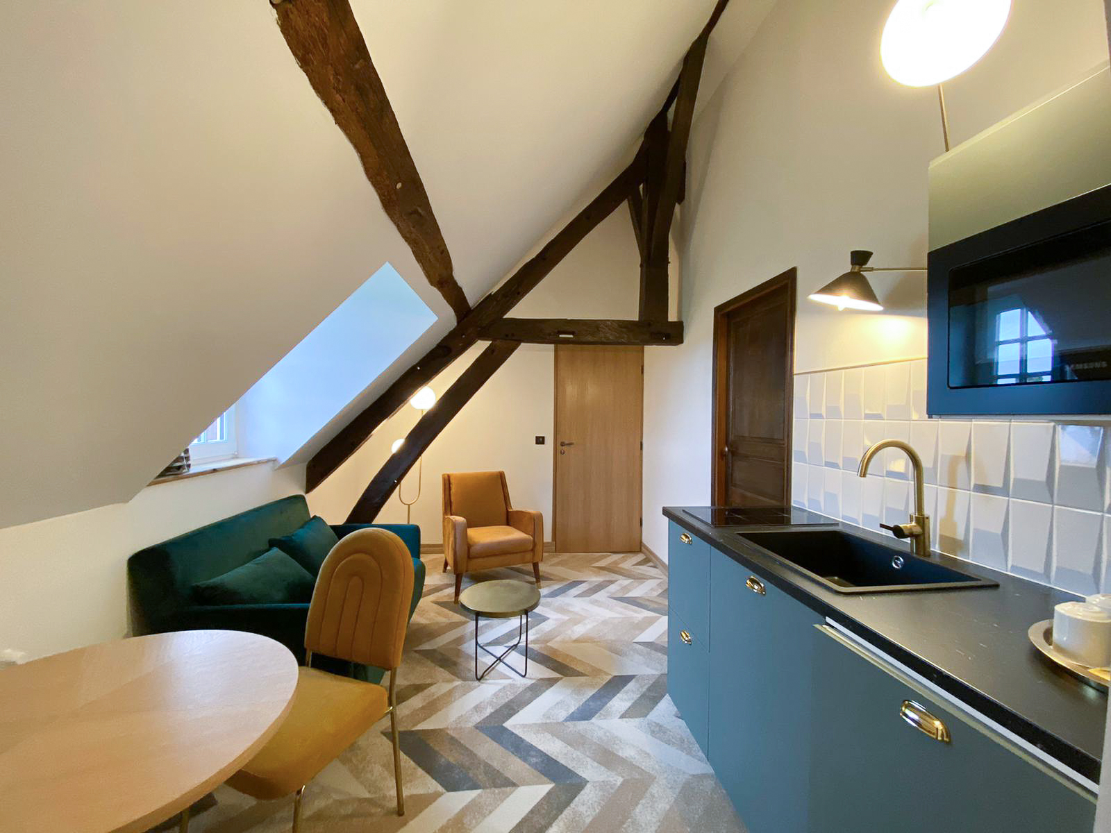 Rénovation d’une maison ancienne en chambre d’hôtes, esprit art déco, kitchenette verte et salon velours vert et doré, laiton Rénovation d’une maison ancienne en chambre d’hôtes au Merlerault dans le perche normand, esprit art déco, espace salon avec un canapé en velours vert, des chaises en velours doré, et kitchenette verte de gris avec poignées laiton et crédence en relief blanche