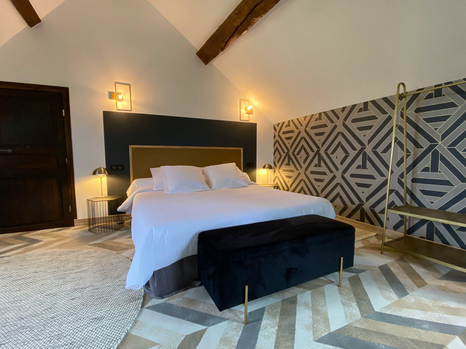 Rénovation d’une maison ancienne en chambre d’hôtes, esprit art déco, papier peint geométrique, laiton, velours et doré Rénovation d’une maison ancienne en chambre d’hôtes au Merlerault dans le perche normand, esprit art déco avec une tête de lit en papier peint à motifs géométriques dorés encadré par des moulures dorées, le tout sur un mur gris foncé