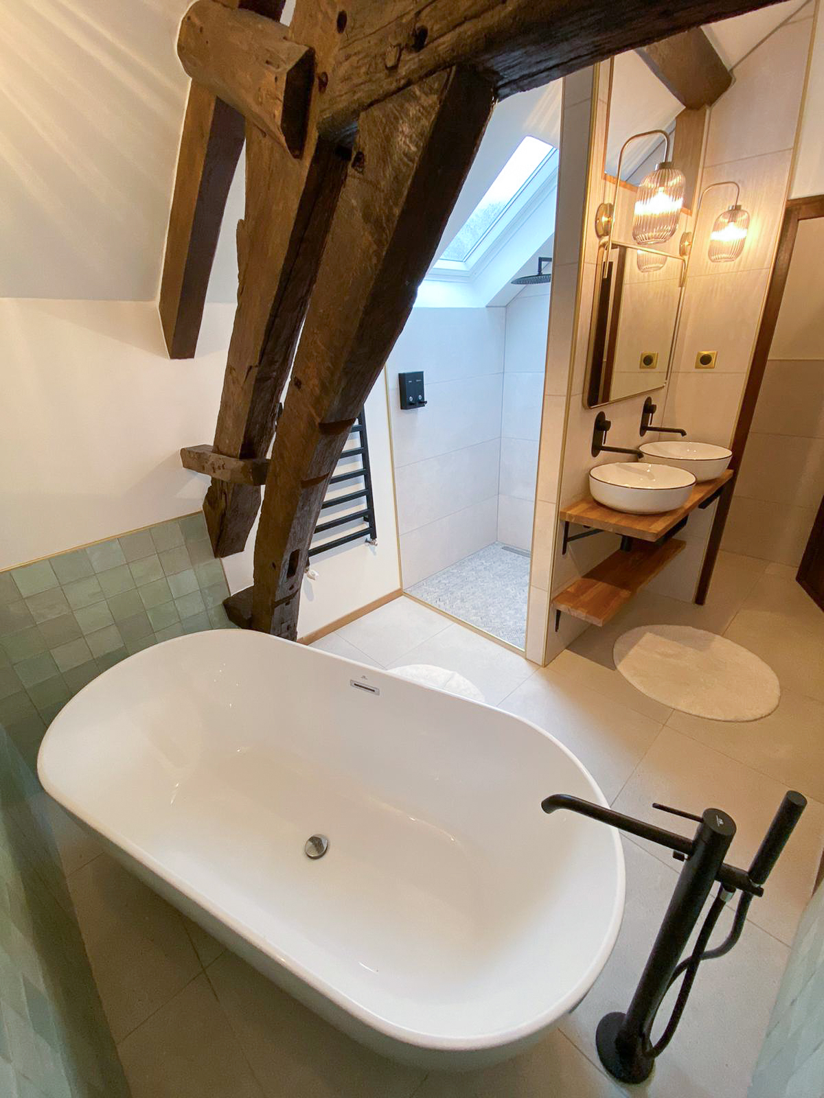 Rénovation d’une maison ancienne en chambre d’hôtes, salle de bain baignoire ilot zelliges vert pastel, douche à l’italienne Rénovation d’une maison ancienne en chambre d’hôtes au Merlerault dans le perche normand, salle de bain avec baignoire ilot entourée de zelliges vert pastel aux murs, douche à l’italienne, plan double vasque bois, vasque à poser blanche, appliques en verre et laiton
