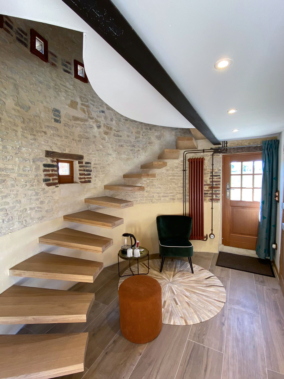 Domaine de Prestal rénovation ancien pigeonnier, coin salon avec escalier Réhabilitation d'un ancien pigeonnier en chambre d'hôtes, escalier aérien en bois, petit coin salon avec fauteuil en velours vert et pouf en velours côtelé terracotta, détails cuivrés, au Merlerault dans le perche normand