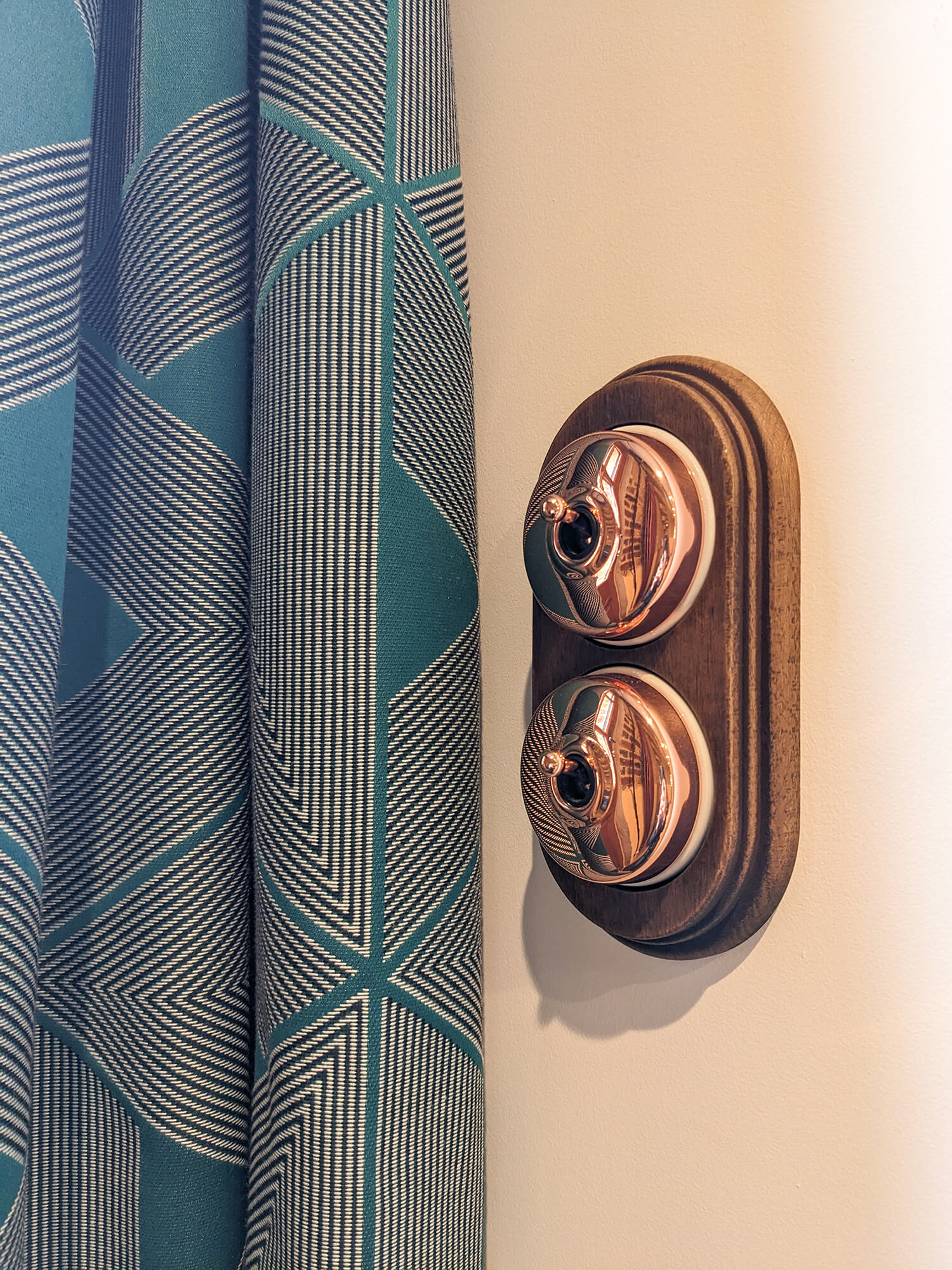 Domaine de Prestal rénovation ancien pigeonnier, détail interrupteur bois et cuivre, rideaux motifs geometriques bleu Réhabilitation d'un ancien pigeonnier en chambre d'hôtes, détail interrupteur bois et cuivre, rideaux bleu motifs géométriques, au Merlerault dans le perche normand
