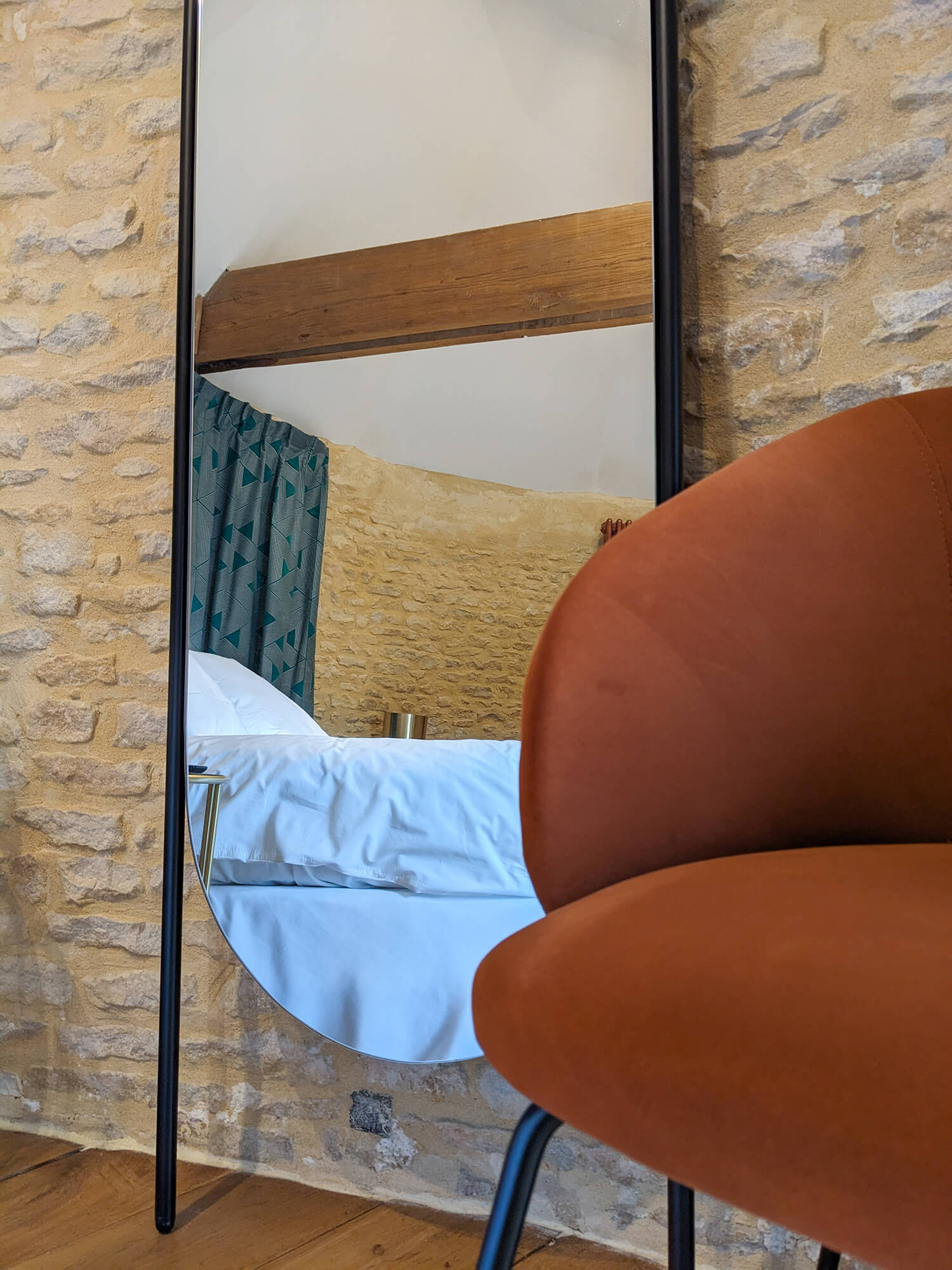 Réhabilitation d'un ancien pigeonnier en chambre d'hôtes, détail miroir métal noir avec fauteuil en velours couleur rouille, mur de pierre, au Merlerault dans le perche normand