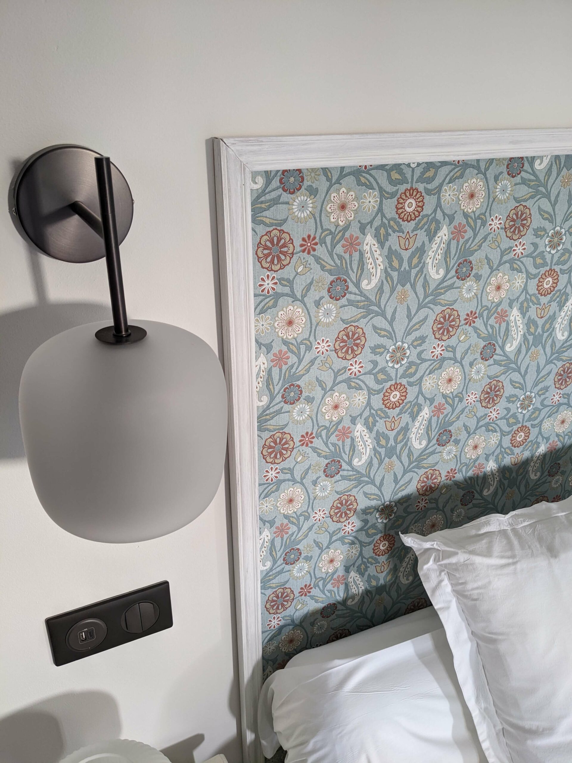 Rénovation d’une maison ancienne en chambre d’hôtes, esprit campagne classique avec une tête de lit en papier peint floral bleu Rénovation d’une maison ancienne en chambre d’hôtes au Merlerault dans le perche normand, esprit campagne classique avec une tête de lit en papier peint floral bleu encadré de moulures et une suspension en verre dépoli