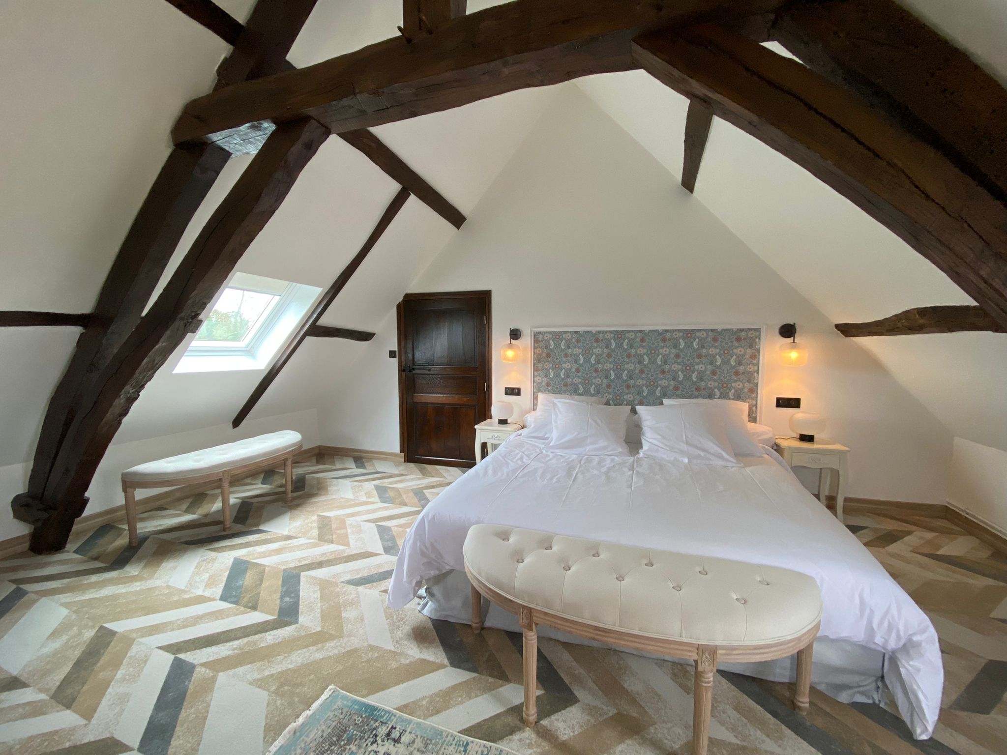 Rénovation d’une maison ancienne en chambre d’hôtes, esprit campagne classique, banquette bout de lit en bois patiné et tissu capitonné Rénovation d’une maison ancienne en chambre d’hôtes au Merlerault dans le perche normand, esprit campagne classique, lit avec banquette en bout de lit en bois patiné et tissu capitonné, tête de lit en papier peint floral bleu entouré de moulures patinées blanches
