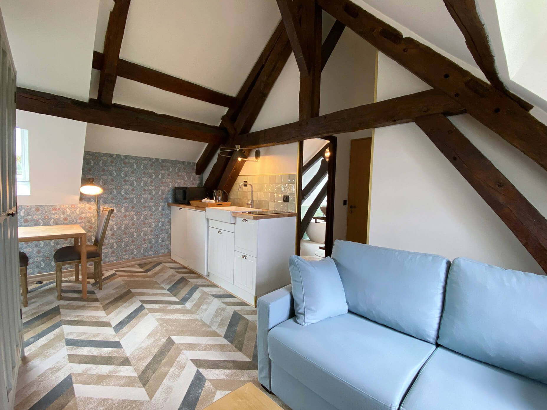 Rénovation d’une maison ancienne en chambre d’hôtes, esprit campagne classique, kitchenette et salon Rénovation d’une maison ancienne en chambre d’hôtes au Merlerault dans le perche normand, esprit campagne classique avec des couleurs pastel, kitchenette avec crédence zelliges vert d’eau, papier peint floral bleu et table bois, canapé bleu ciel