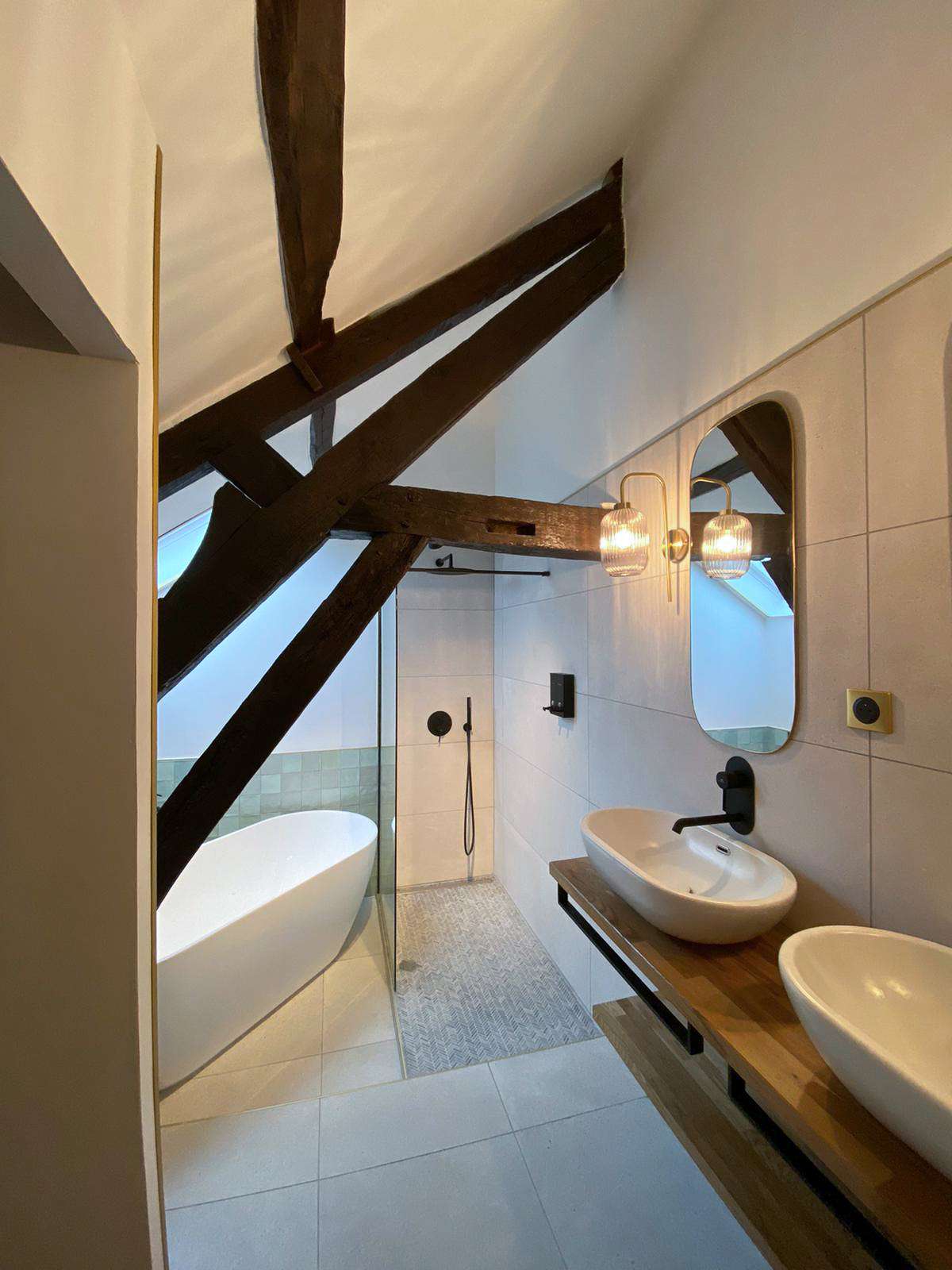 Rénovation d’une maison ancienne en chambre d’hôtes, salle de bain baignoire ilot zelliges vert pastel, douche à l’italienne Rénovation d’une maison ancienne en chambre d’hôtes au Merlerault dans le perche normand, salle de bain avec baignoire ilot entourée de zelliges vert pastel aux murs, douche à l’italienne, plan double vasque bois, vasque à poser blanche, appliques en verre et laiton