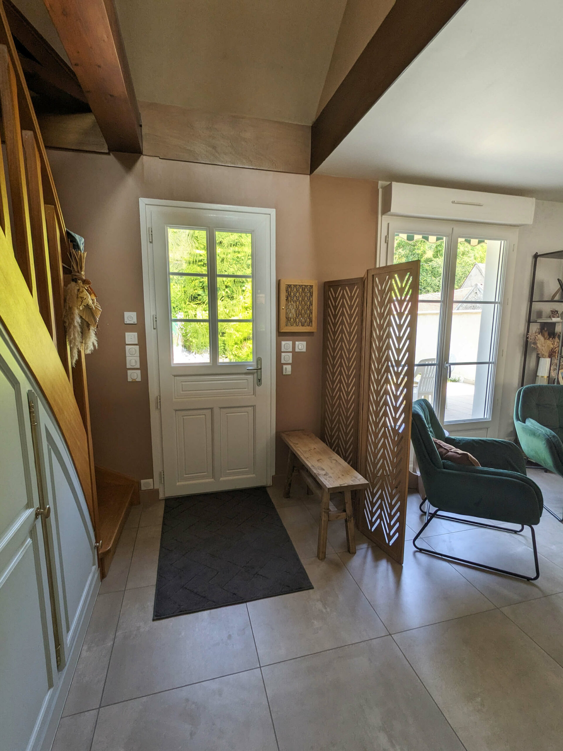 Rénovation d’une maison familiale en campagne essonnienne à Chalo-Saint-Mars, vue sur l’entrée avec poutres en bois apparentes, suspension boule en bois, paravent et banc en bois, mur terracotta et fauteuil en velours vert sapin