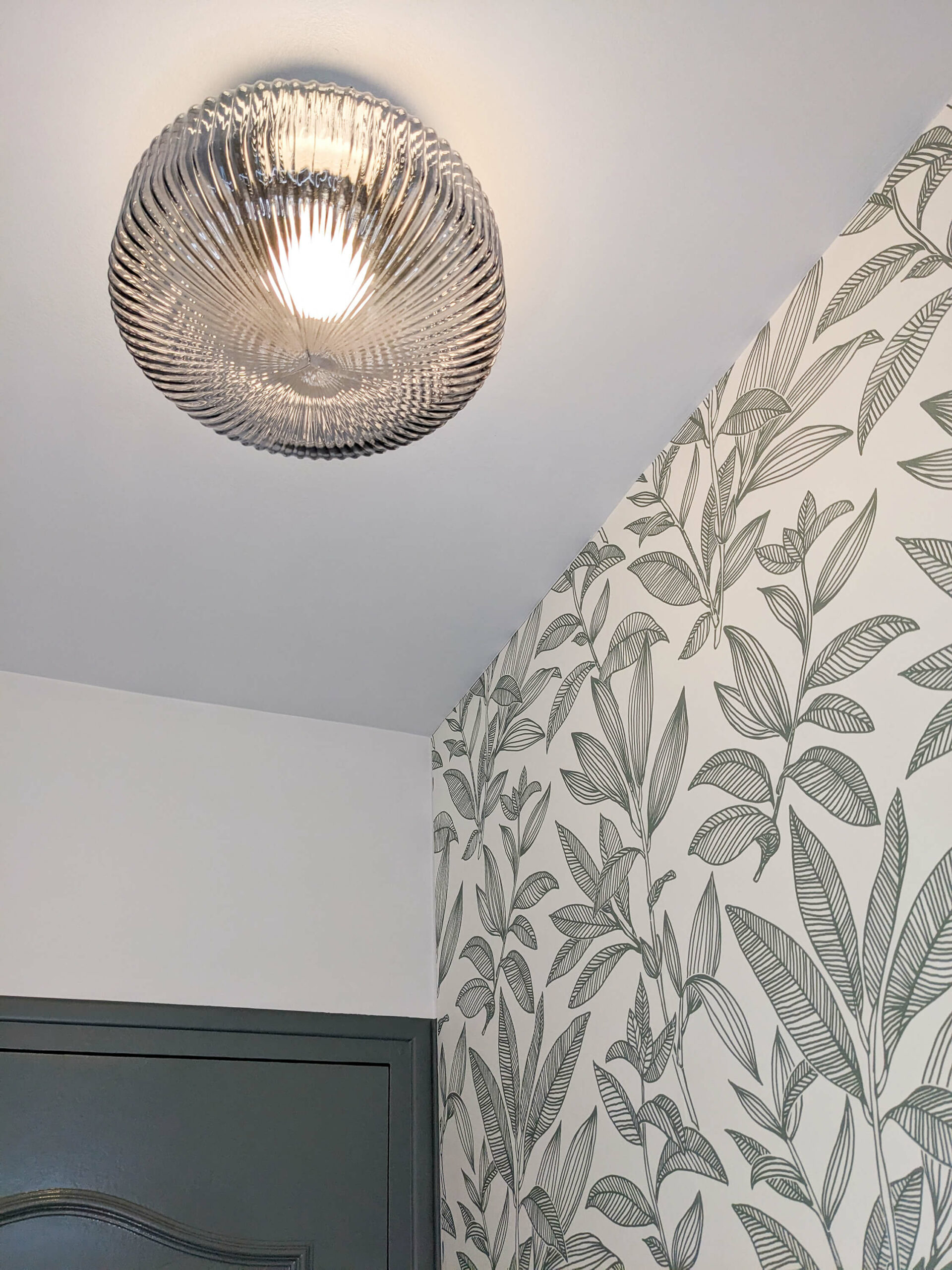 Rénovation d’une maison familiale en campagne essonnienne à Chalo-Saint-Mars, décoration de toilettes style maison ancienne de campagne avec un soubassement en moulures de couleur vert, un papier peint sobre avec des feuilles vertes et un plafonnier en verre ambré flûté et laiton