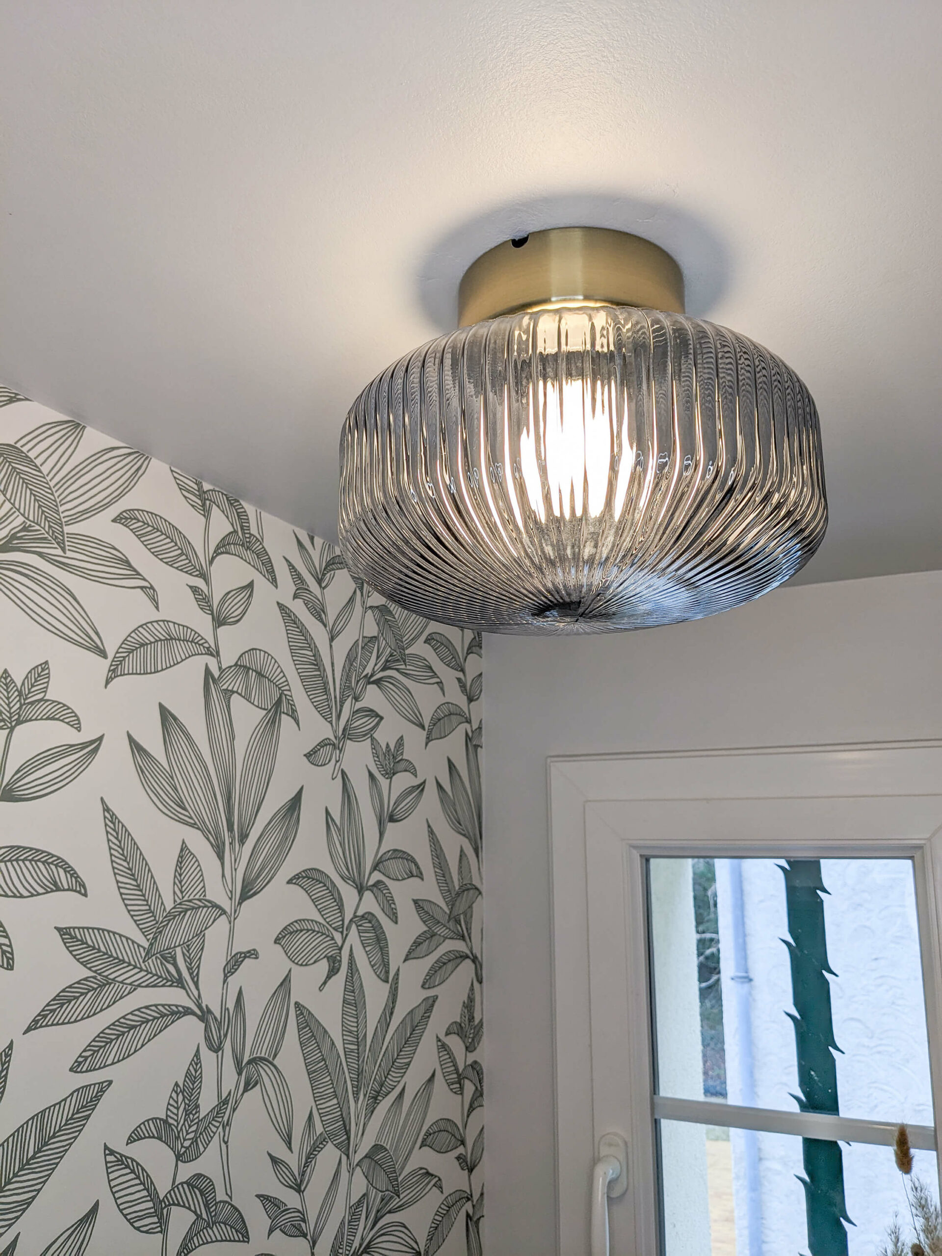 Rénovation d’une maison familiale en campagne essonnienne à Chalo-Saint-Mars, décoration de toilettes style maison ancienne de campagne avec un papier peint sobre avec des feuilles vertes et un plafonnier en verre ambré flûté et laiton