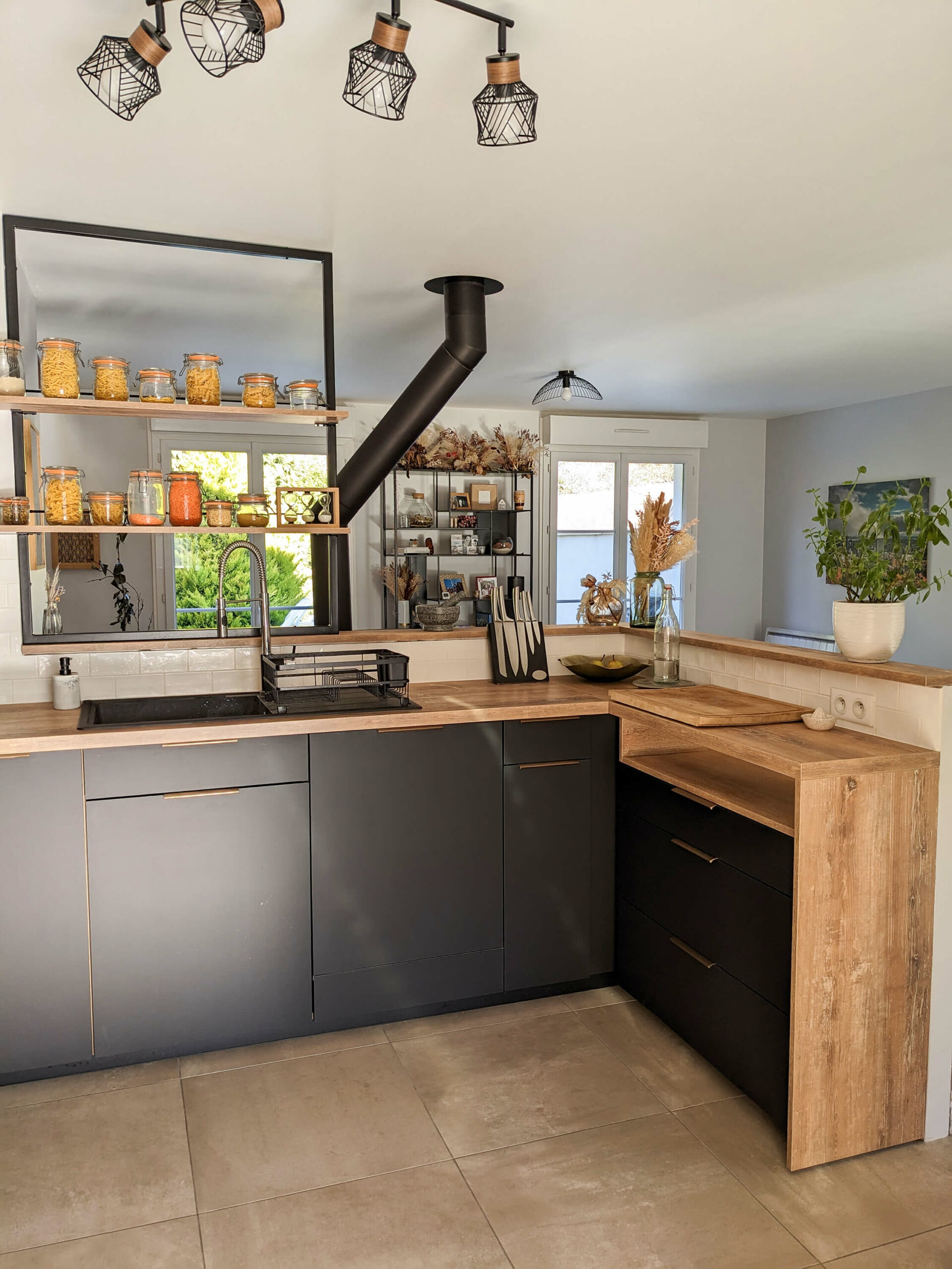 Rénovation d’une maison familiale en campagne essonnienne à Chalo-Saint-Mars, une cuisine complètement rénovée et semi ouverte sur le séjour. Facades noir mat avec du bois rustique profond, étagères et cadre métallique noir sur mesure