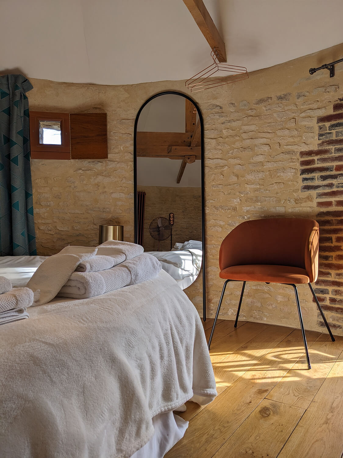 Réhabilitation d'un ancien pigeonnier en chambre d'hôtes, avec poutres apparentes et murs en pierres, lit rond, tête de lit en rideaux à motifs géométriques, détails cuivrés, au Merlerault dans le perche normand