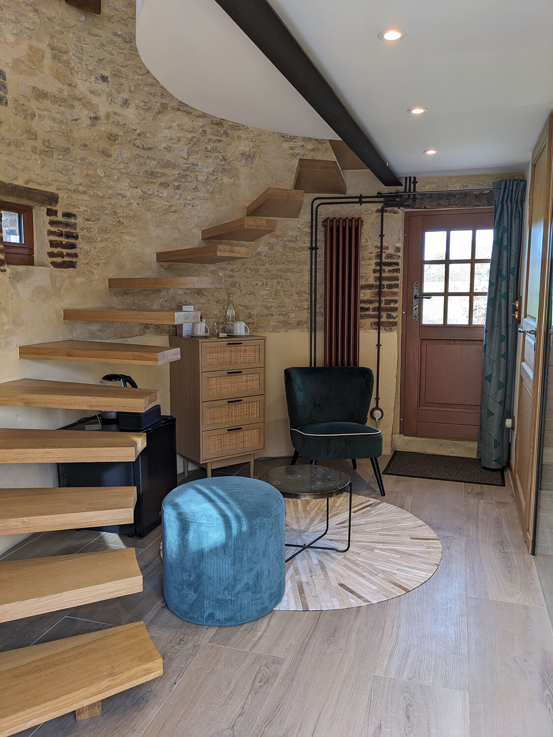 Réhabilitation d'un ancien pigeonnier en chambre d'hôtes, escalier aérien en bois, petit coin salon avec fauteuil en velours vert et pouf en velours côtelé terracotta, détails cuivrés, au Merlerault dans le perche normand