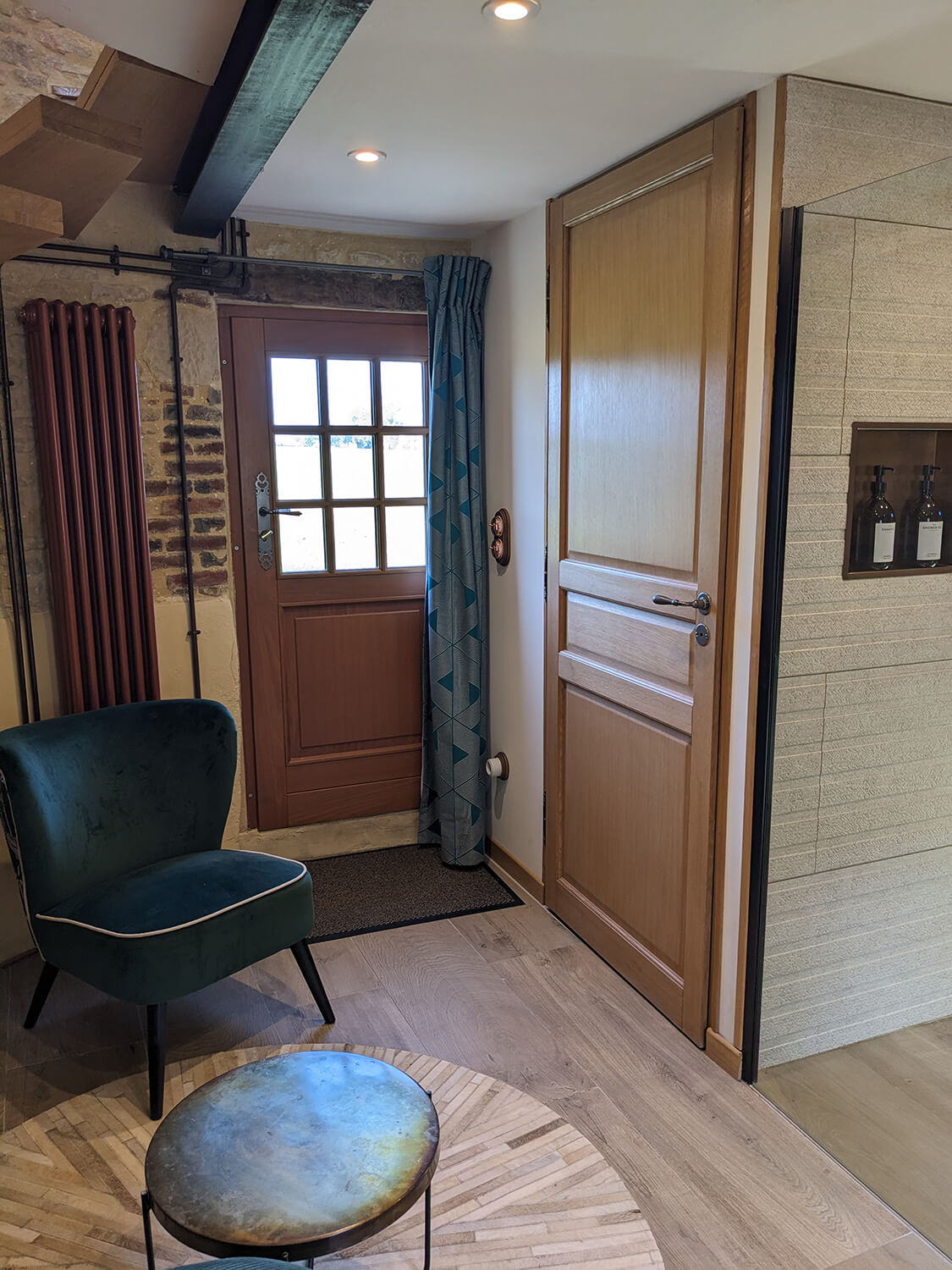 Réhabilitation d'un ancien pigeonnier en chambre d'hôtes, escalier aérien en bois, petit coin salon avec fauteuil en velours vert et pouf en velours côtelé terracotta, détails cuivrés, au Merlerault dans le perche normand
