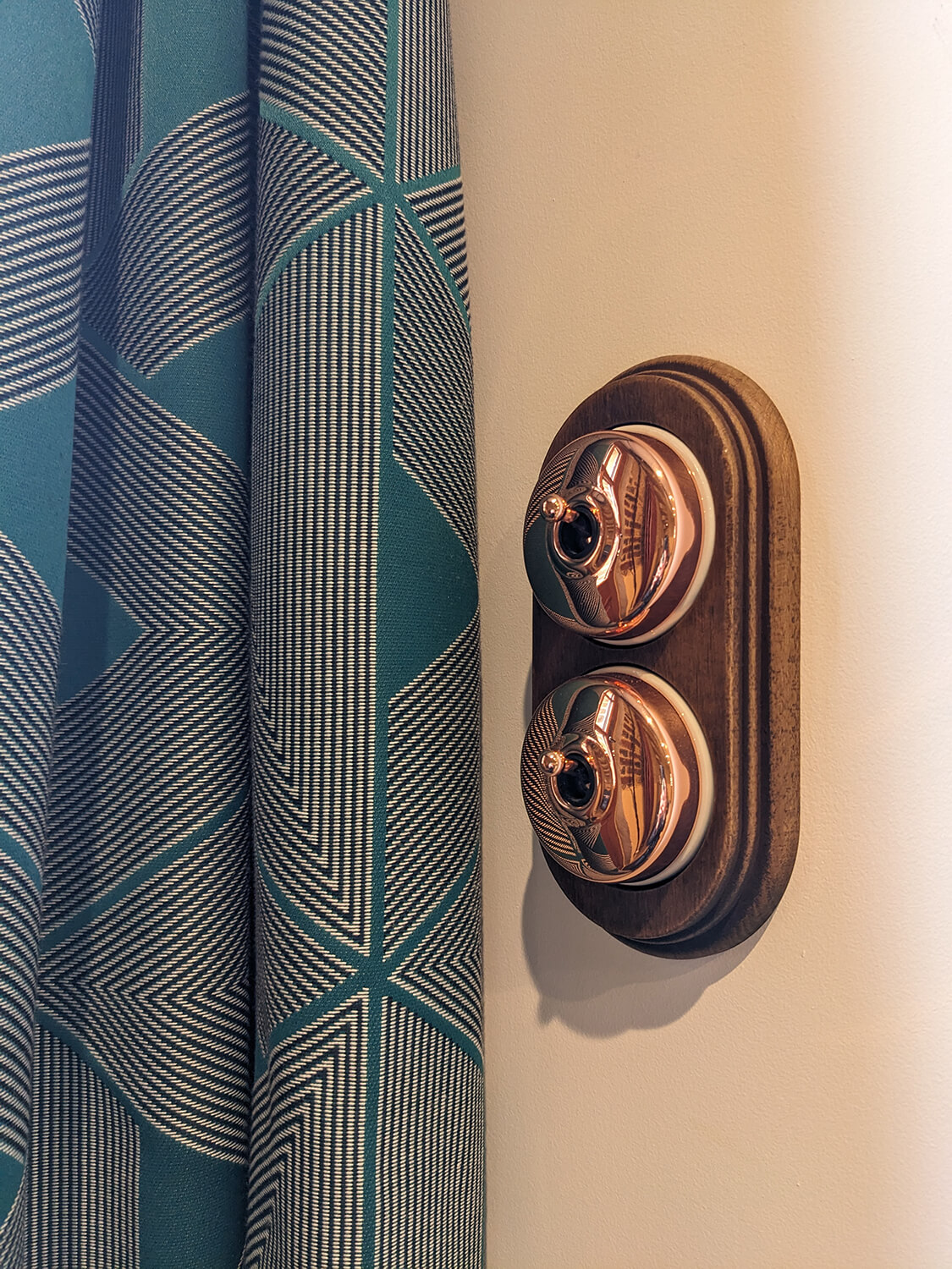 Réhabilitation d'un ancien pigeonnier en chambre d'hôtes, détail interrupteur bois et cuivre, rideaux bleu motifs géométriques, au Merlerault dans le perche normand