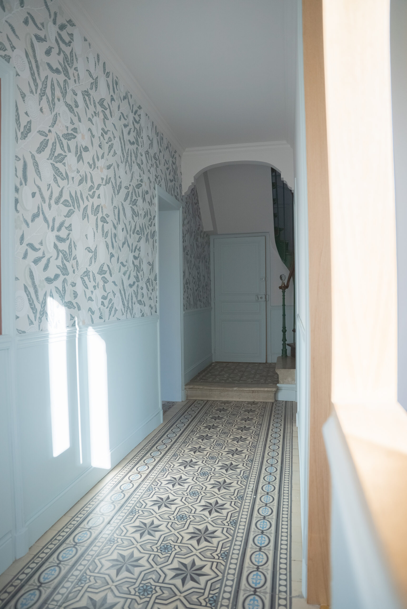 Rénovation d’une maison meulière à Bonnières, retrouver le charme de l’ancien, entrée avec les carreaux de ciment d'origine conservés, les soubassements peints en bleu ciel et un grand linéaire de papier peint aux mélanges de fleurs bleutées