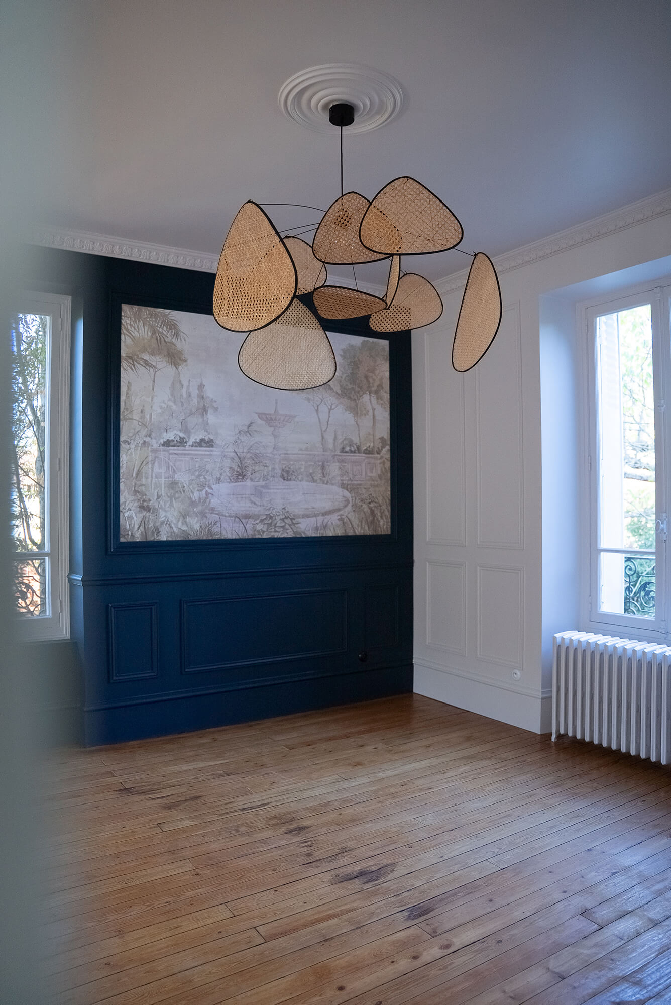 Rénovation d’une maison meulière à Bonnières, retrouver le charme de l’ancien, salle à manger avec mur un bleu profond mouluré, un papier peint encadré, des corniches au plafond et des cimaises sur tous les murs, une suspension XXL Screen en cannage