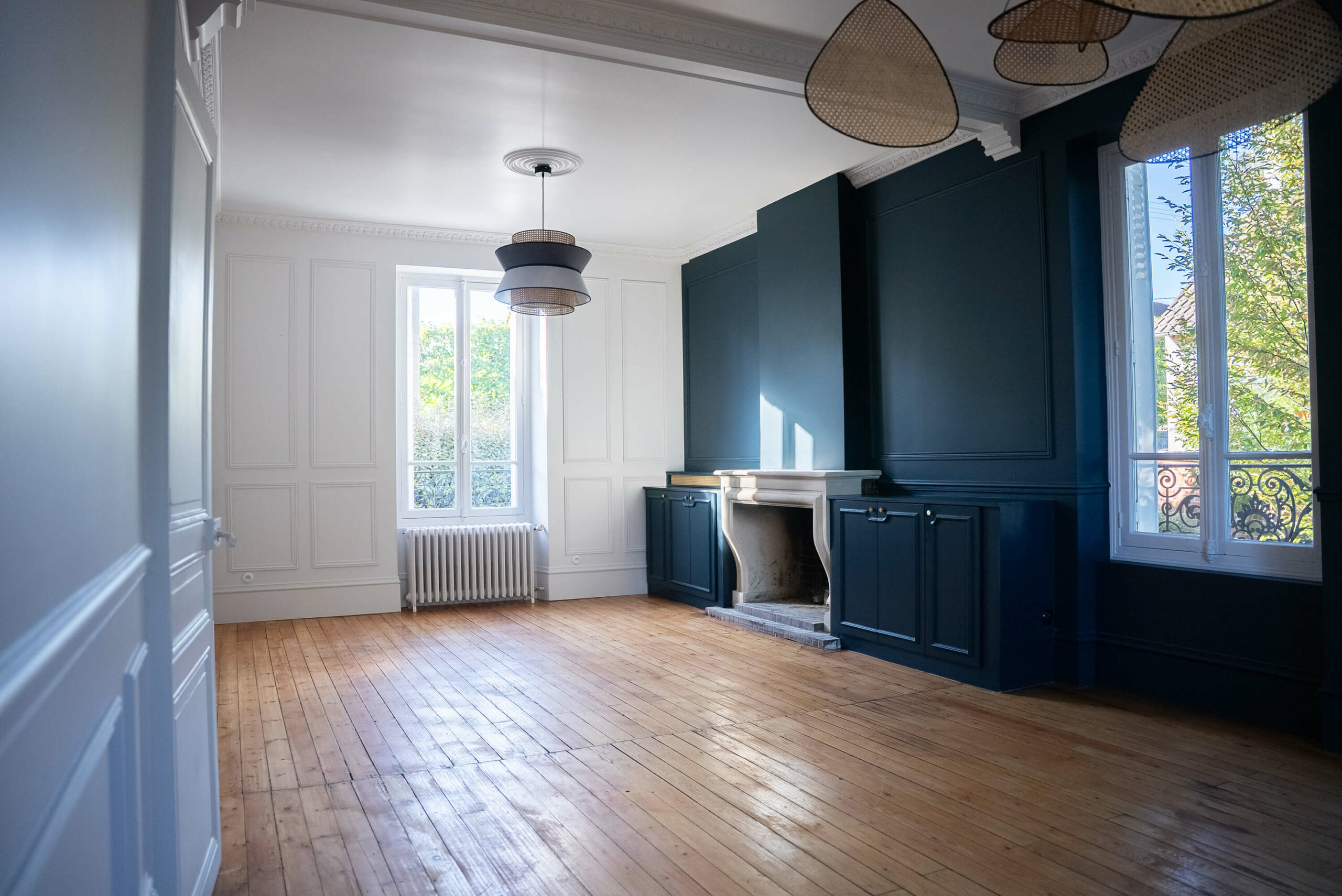 Rénovation d’une maison meulière à Bonnières, retrouver le charme de l’ancien, salon cheminée avec des agencements sur mesure peint en bleu profond comme le mur, des corniches au plafond et des cimaises sur tous les murs, le parquet ancien est conservé