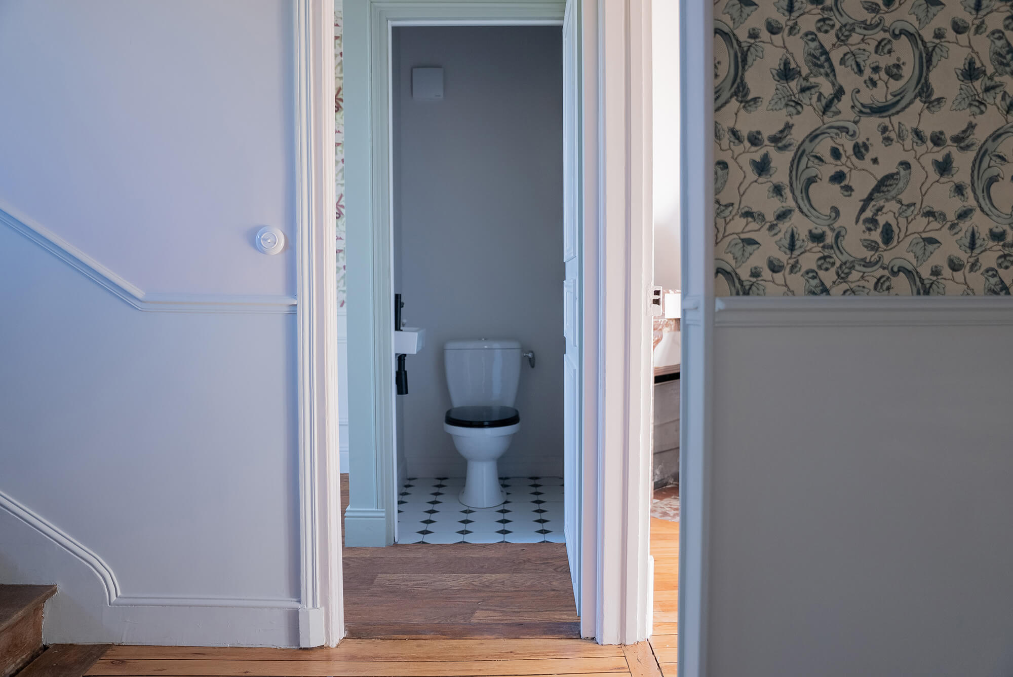 Rénovation d’une maison meulière à Bonnières, retrouver le charme de l’ancien, palier avec soubassement bleu clair et cimaises, papier peint effet toile de jouy bleu, toilettes avec carrelage cabochon noir et blanc