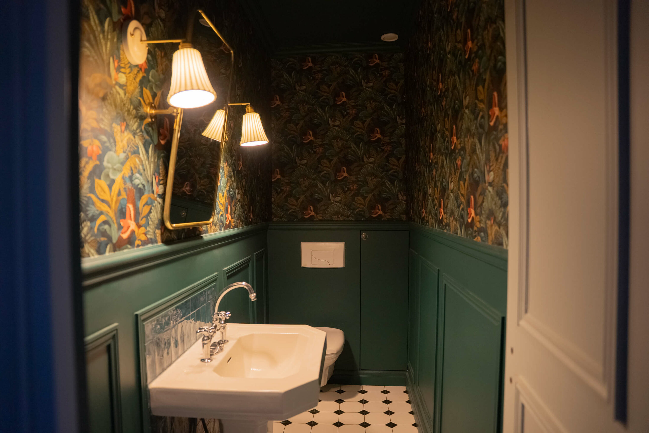 Rénovation d’une maison meulière à Bonnières, toilettes cabinet de curiosité avec murs moulurés vert foncé et papier peint tropical